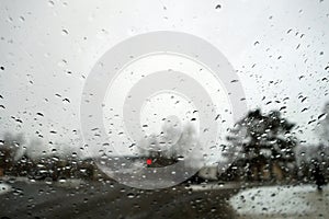 View on winter road through wet windshield with rain drops