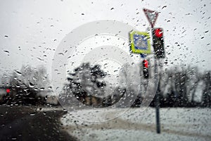 View on winter street and traffic lite through wet windshield with rain drops