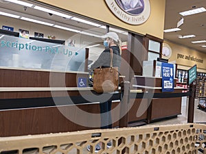 Kirkland, WA USA - circa October 2021: View of a woman in a baseball hat picking up a prescription at a pharmacy inside a Safeway