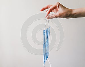 View of a woman hand holding face mask over white textured table background. Protective respiratory mask for spreading virus. Clo