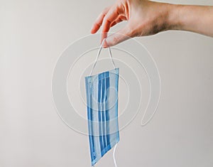 View of a woman hand holding face mask over white textured table background. Protective respiratory mask for spreading virus. Clo