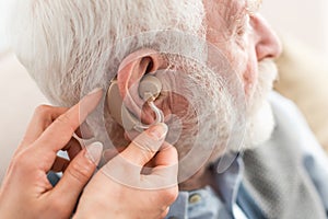 View of woman helping grey haired man, wearing hearing aid
