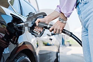 View of woman holding fuel pump while refueling car with benzine