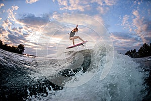 View of woman jumping over big splashing wave on surf style wakeboard.