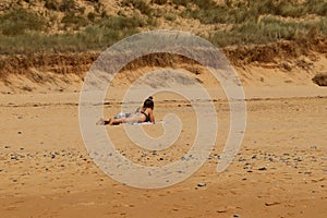 View of a woman lying and sunbathing on sandy beach on sunny day in Brittany in France.