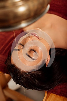 View of woman lying under shirodhara vessel during ayurvedic procedure