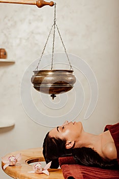 View of woman lying under shirodhara vessel during ayurvedic procedure photo