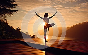 View of a woman practicing yoga positions and stretching in front of a beautiful lake landscape at sunset