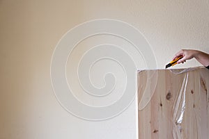 View of woman`s hand with cutter unpacking a pine board, on a wall