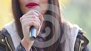 View of woman's mouth with red lipstick, smiling and singing with microphone