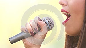 View of woman's mouth with red lipstick, smiling and singing with microphone