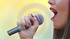View of woman's mouth with red lipstick, smiling and singing with microphone