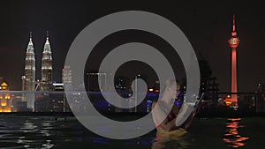 View of woman in swimming pool on the skyscraper roof making selfie by tablet against night city landscape. Kuala Lumpur