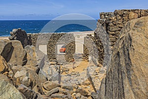 View of woman walking inside Bushiribana ruins toward her red vehicle. Blue water of Atlantic Ocean on background.