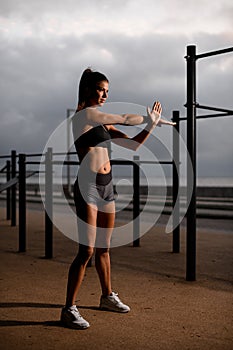 view on woman warming-up muscles before workout doing stretching exercise outdoor.