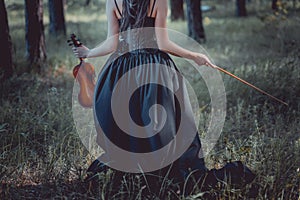 View of woman in witch costume walking on forest, holding violin