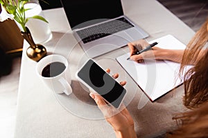 View of woman working with notepad, smartphone and laptop in cafe