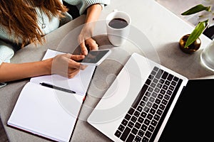 View of woman working with notepad, smartphone and laptop in cafe with coffee cup