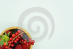 View of a wooden bowl filled with strawberries, blackberries, raspberries, redcurrants and blueberries in the lower left corner.