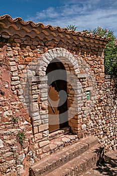 View of wooden door and wall and arch in stone under a sunny blue sky, in Roussillon.