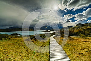 View of a wooden path and mountains in the Torres del Paine National Park on a cloudy day. Autumn in Patagonia, the