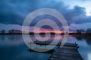 View from a wooden pier on a calm lake during sunset with dark clouds