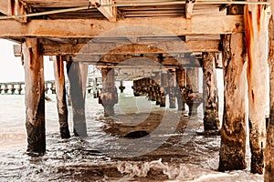 View of wooden under pier bridge over waves of sea