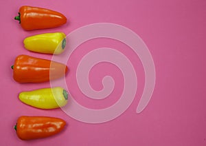 View on yellow and orange color rew sweet mini bell peppers in a row with blank pink background for text copy space photo