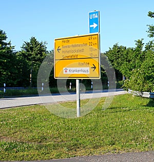View of yellow traffic direction sign to city in Germany with trees and clear blue sky background