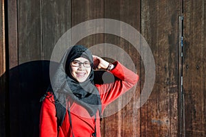 View of young Asian muslim woman wearing black hijab and red coat leaning on ancient wooden gate in Kyoto