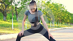 View on young athletic woman in sportswear does stretching exercises outdoor.