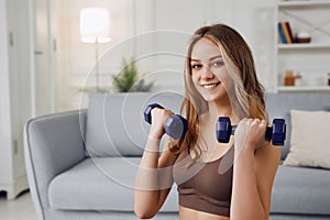 View of a young attractive girl doing exercise at home with dumbells. Healthy lifestyle.