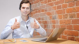 View of a Young attractive man working on laptop showing thumbs up, call center