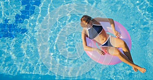 View of young brunette woman swimming on the inflatable pink ring