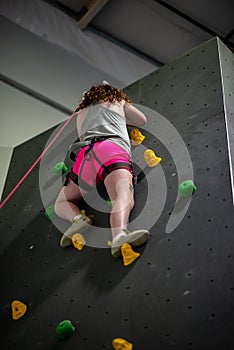 Young girl climbing up on practice wall in indoor rock gym