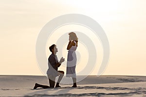 View of young man doing marriage proposal to girlfriend on sandy beach at sunset