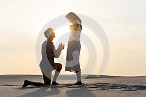 View of young man doing marriage proposal to girlfriend on sandy beach at sunset