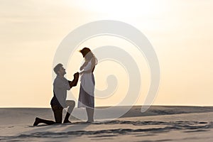 View of young man doing marriage proposal to girlfriend on sandy beach at sunset