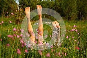 The view of young mother and daughter on green grass background. feet close-up.