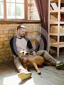 View of young sportive man having fun with dog at home.