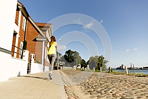 View of young woman running on sidewalk in morning. Health conscious concept