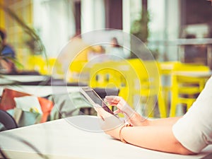 View of a young woman sitting in a cafe holding a smartphone in her hands for online communicating, paying, shopping.