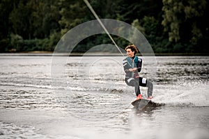 view of young woman in wetsuit riding on river water on wakeboard holding rope with her hands