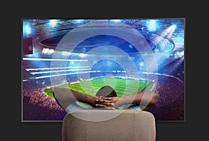 Viewer in front of a large TV relaxed on the armchair at home watching a sports game