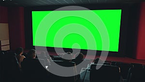 Viewers enjoying movie on big green screen copyspace in dark cinema
