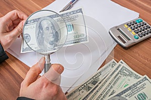 Viewing fake or counterfeit dollar banknote with magnifying glass