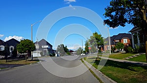 Viewpoint of suburban city street with vehicle traffic. Urban road along residential suburb houses during day
