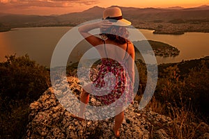 Viewpoints to capture memorable sunsets. Young woman in colorful dress and hat standing upright and watching sunset of the city of