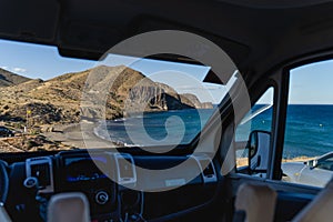 Views of a cliff and a beach with blue sea through the windscreen of a parked motorhome van.