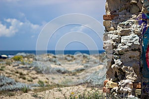 Views of the sea from the beach, the sea is azure blue, as is the sky. Next to it is the wall of some old building demolished.